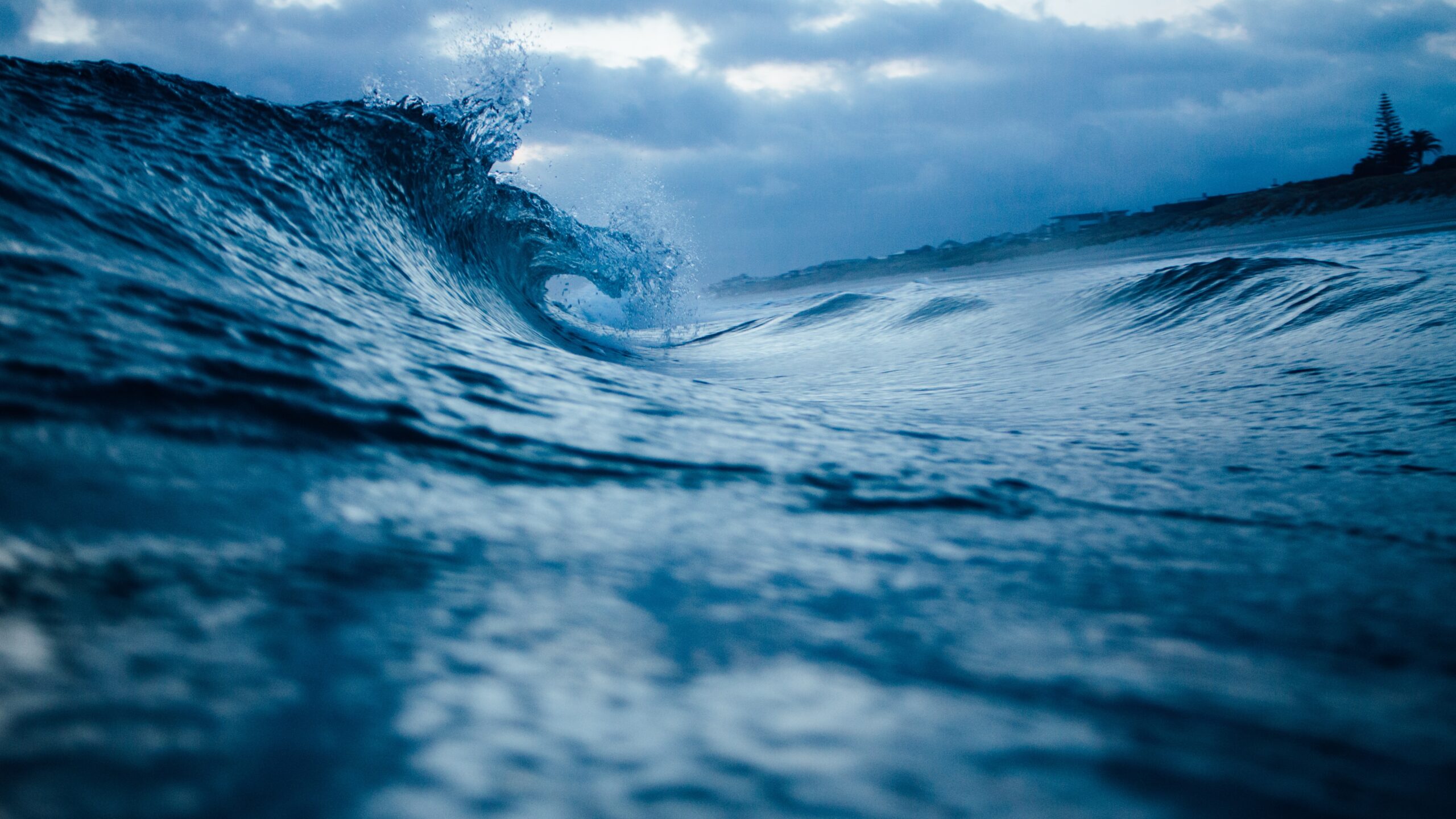 a wave breaks against a sandy shore. There is a lighthouse in the distance.
